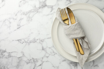 Stylish setting with cutlery, napkin and plates on white marble table, top view. Space for text