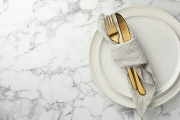 Stylish setting with cutlery, napkin and plates on white marble table, top view. Space for text