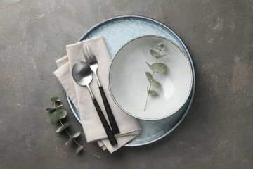 Stylish setting with cutlery, napkin, eucalyptus branches and plate on grey table, top view