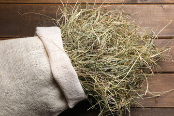 Dried hay in burlap sack on wooden table, top view
