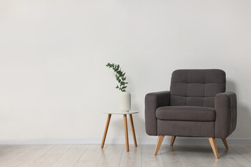 Comfortable armchair, side table and eucalyptus near white wall indoors, space for text