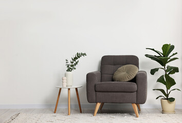 Comfortable armchair, pillow, side table and green houseplants indoors, space for text