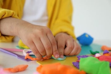 Little girl sculpting with play dough at white table indoors, closeup