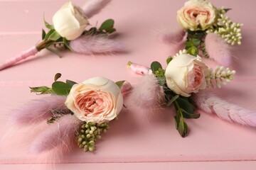 Many small stylish boutonnieres on pink wooden table, closeup