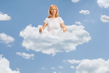 Middle aged woman in white clothes practicing yoga on a cloud