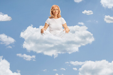Middle aged woman in white clothes practicing yoga on a cloud