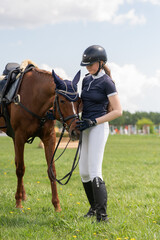 A young girl stands next to a horse before an equestrian competition. Vertical photo.
