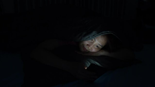 Young Woman Addicted to Social Media, Lying in the Dark Bedroom, Struggling with Insomnia and Strained Eyes from Nighttime Scrolling and Online Shopping