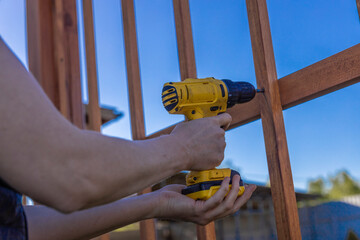 A person in work attire using a power drill to secure a wooden fence panel onto metal posts in a...