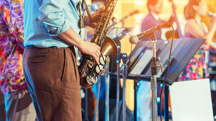 Musician playing saxophone on blurred background. Man with friends blow saxophone with the band for...