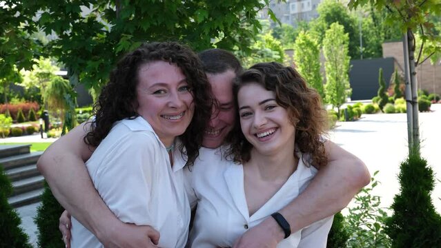 Happy family friends hugs one man two women smiles mother daughter father. Show heart with hands. A man hugs his family on both sides in a tight hug.