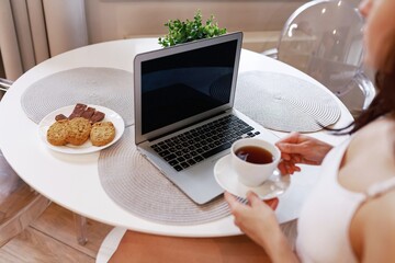 Pretty woman wearing white lingerie and sitting at the table at home while looking at laptop...