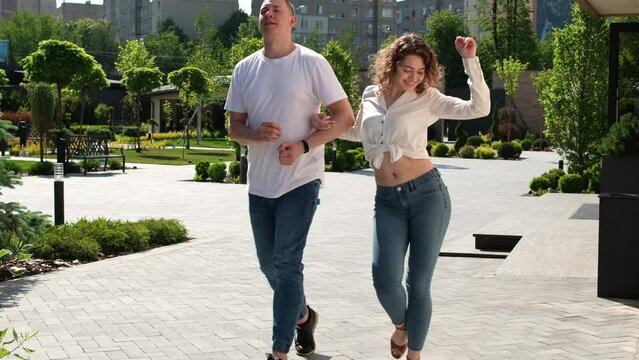 guy and a girl walk funny arm in arm and look at the camera, pose, smile, make eyes, a couple walks along the street. Falling in love sexuality adults young people