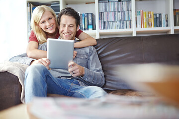 Happy, couple and hugging in lounge with tablet, relax online and people smile for internet browse together. Social media, web and scrolling for relationship bonding, networking and apartment