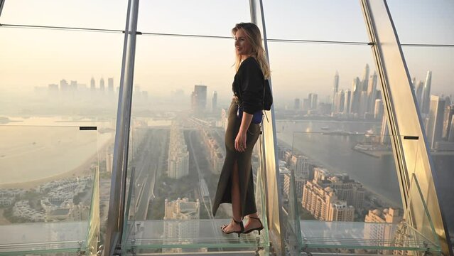 A woman is seen standing at the top of a tall building during a Dubai sunrise, showcasing the cityscape below