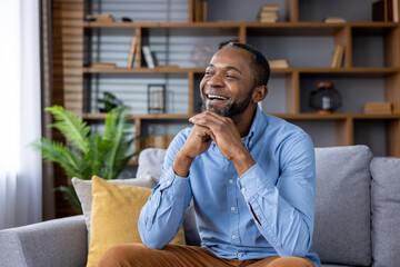 A cheerful man is relaxing on a sofa at his home. The modern living room is welllit and organized,...