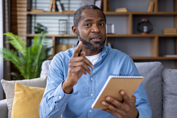 A man speaks confidently with a notebook in a modern home office. The background consists of a...