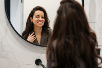 Happy attractive woman in silk robe looking at mirror in bathroom, enjoying the morning at home. Beauty, lifestyle, morning routine concept