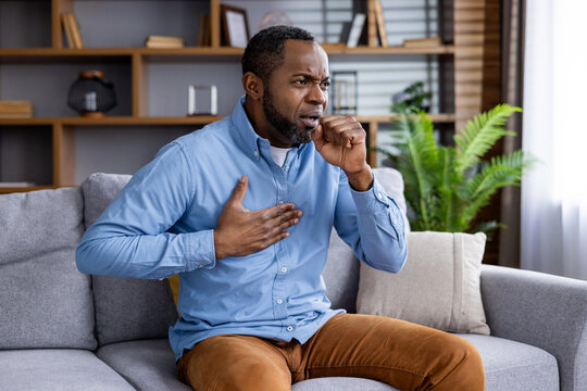 Man at home in distress, clutching chest, coughing may have severe respiratory illness. Urgent medical help needed. Symptoms chest pain, difficulty breathing, coughing fits serious