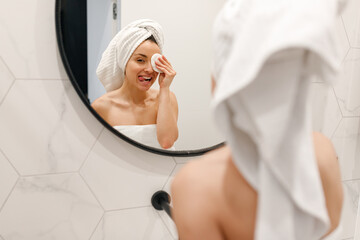 Happy beautiful lady having fun and removing makeup with cotton pad, standing in the bathroom,...