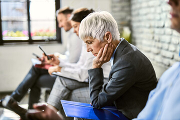 Mature  businesswoman feeling worried while waiting for job interview with other candidates.