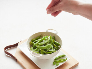 womans hand seasoning with coarse sea salt on boiled edamame soybeans