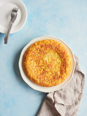 Homemade potato omelette, typical Spanish food called tortilla de patata, served whole on plate on blue background.