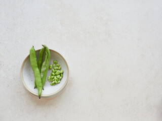 Raw fresh green fava beans, broad bean, pods in a ceramic bowl on the countertop, top view with copy space.