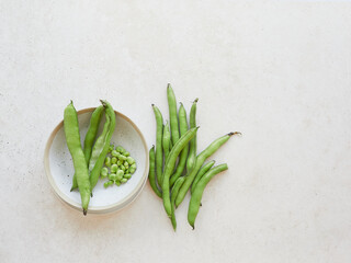 Fresh green fava beans, broad bean or vicia faba. Pods freshly harvested on light stone countertop and some shelled in a ceramic bowl.