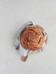 Top view of a delicious loaf of freshly baked crusty homemade bread placed on a dish towel and wooden board on the kitchen counter.