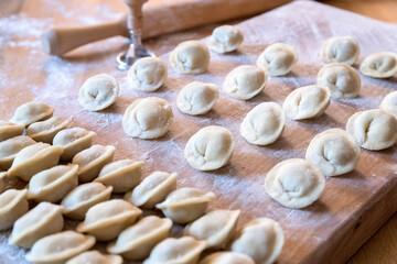 The raw dumplings were placed on a wooden cooking board. Next to it is a rolling pin for rolling out the dough and a tool for cutting the dough. Modeling dumplings by hand.