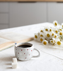 Front view: a cup of hot coffee, with sugar cubes, standing on the kitchen table in the morning light. The concept of a homemade breakfast.