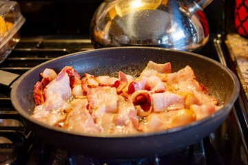 A pound of thick cut bacon frys in a skillet on a gas stove top.