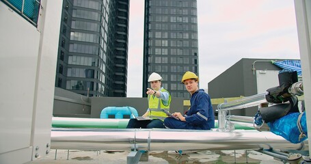 civil engineer Construction manager and manual worker inspector foreman in safety helmet holding laptop meeting conversation about project work at rooftop of building construction site