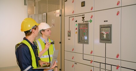 Obraz premium Two electricians electrical engineers in protective uniform checking voltage control panel screen system at electrical cabinet for generate electricity of factory in manufacture industrial