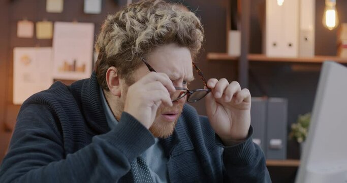 Loop of shocked entrepreneur putting on glasses and staring at unbelievable project results on computer screen in office in evening. Business and emotion concept.