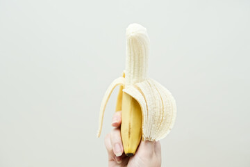 Woman's hand holding peeled banana fruit. On a white wall background isolated. Studio photo....