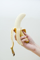 Woman's hand holding peeled banana fruit. On a white wall background isolated. Studio photo. Healthy eating, lifestyle concept.