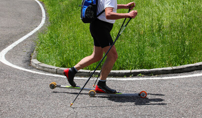 adult skier with ski Roller on asphalt road and poles for training