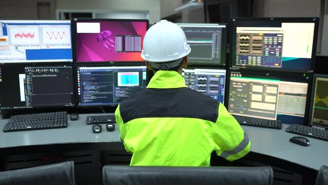 Engineer working in a control room,programming to manage industrial machines,monitoring multiple screens,efficient workflow