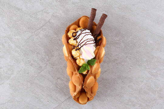 Trendy Hong Kong bubble waffles with ice cream, cream and berries on white wooden background. Copy space