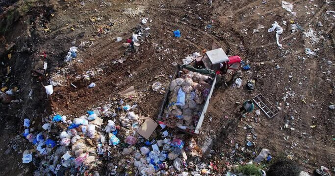 Garbage transportation by tractor pulling a trailer on rural road. Landfill dumping illegal activity, aerial view