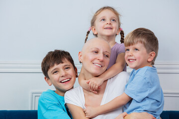 A smiling bald mother enjoys warm supporting hug from her kids