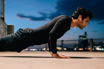 Young sport motivated man pushing up from ground during evening workout in urban setting.Fit man...