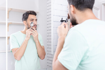 Handsome man doing facial workout with spoon exercises in front of the mirror. Young guy holding...