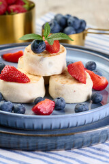 Round small fried cheesecakes on a blue plate with berries. Healthy breakfast