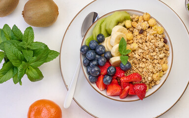 Granola with strawberries, kiwi, banana and blueberries in a round plate on a white table. Healthy...