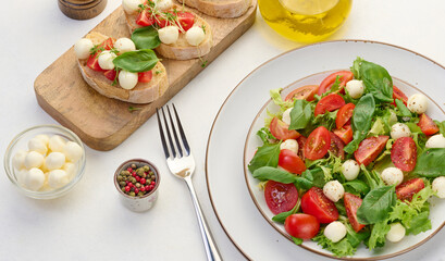 Salad with mozzarella, cherry tomatoes and green lettuce in a white round plate on the table