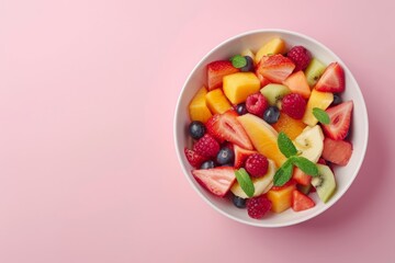 Fruit salad in a bowl on a pink background with copy space, in a top view. A fresh healthy food concept. colorful fruit bowl filled with tropical fruits in a white plate. fresh summer dish