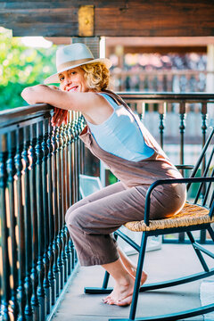A woman is relaxing on a rocking chair on a balcony.